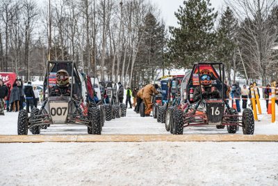 Baja cars lined up at a snowy starting line.